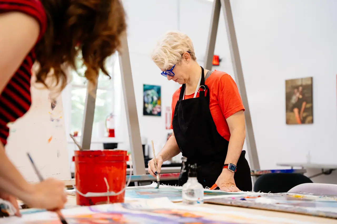 Woman in a red shirt painting at a table during a class